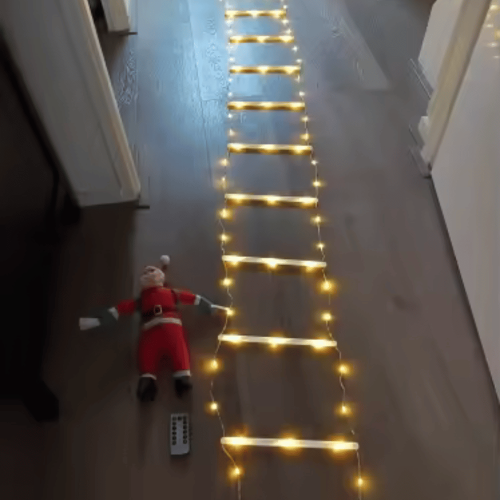 Santa Claus toy lying on a floor with string lights arranged in a ladder pattern.